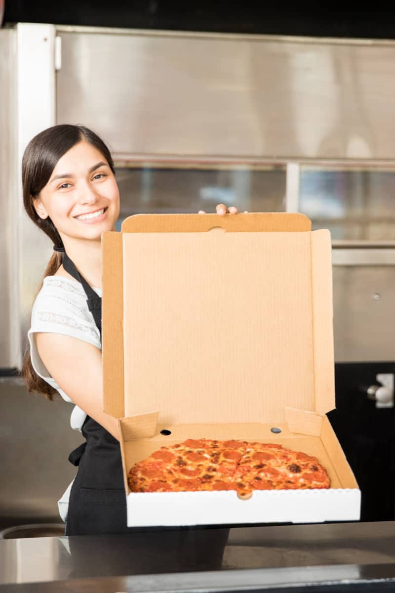 A lady packaging a pizza in a box for delivery